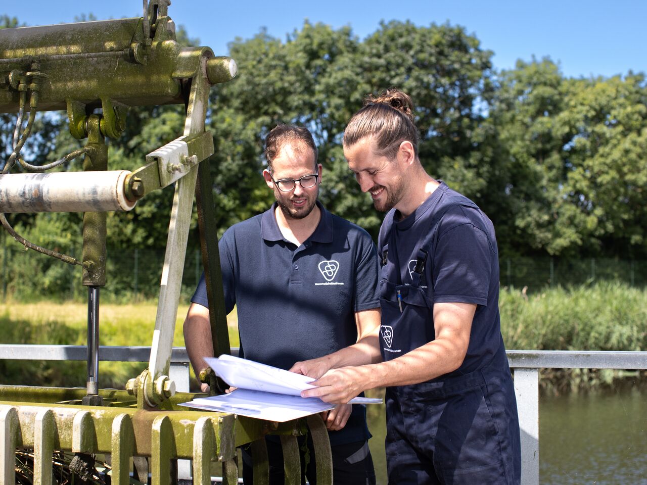 twee collega's staan buiten lachend op de foto en kijken naar een werkblad. 