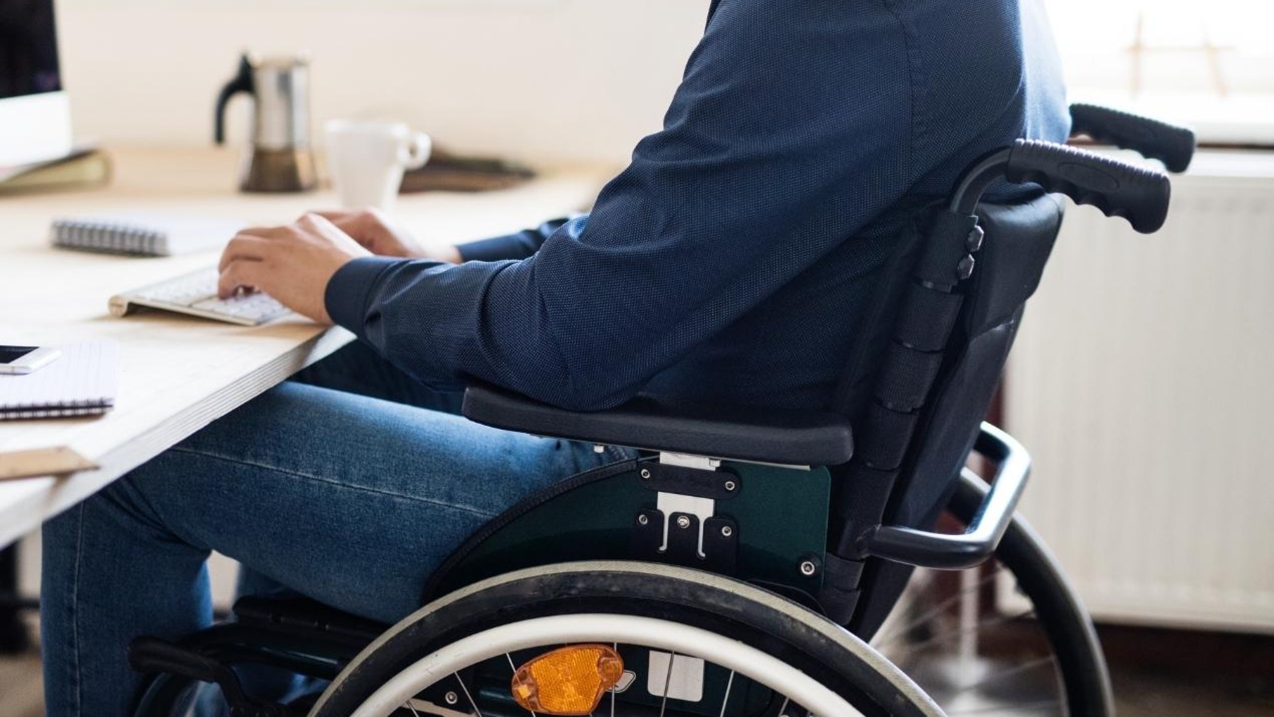 Een foto van een persoon in een rolstoel achter een bureau.