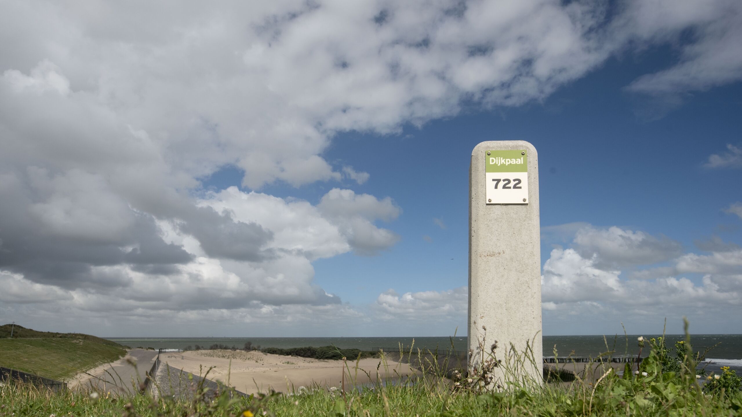 Een dijkpaal bovenop een dijk tegen een bewolkte lucht.