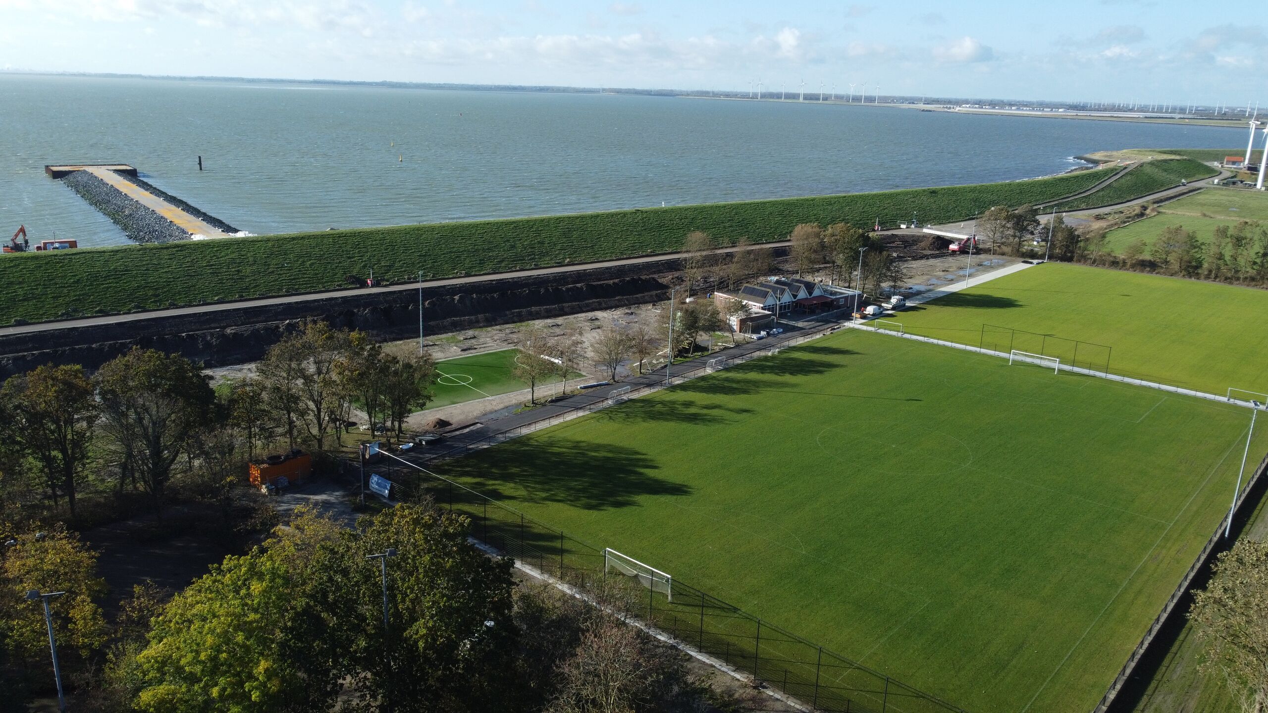 Een dijk met op de voorgrond twee groene voetbalvelden achter is een tijdelijke aanlandig in de Westerschelde te zien.