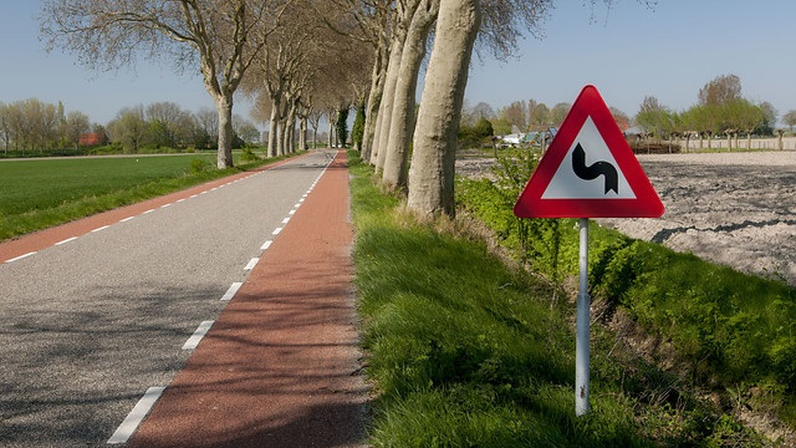Waterschapsweg met bomen en verkeersbord haakse bocht.