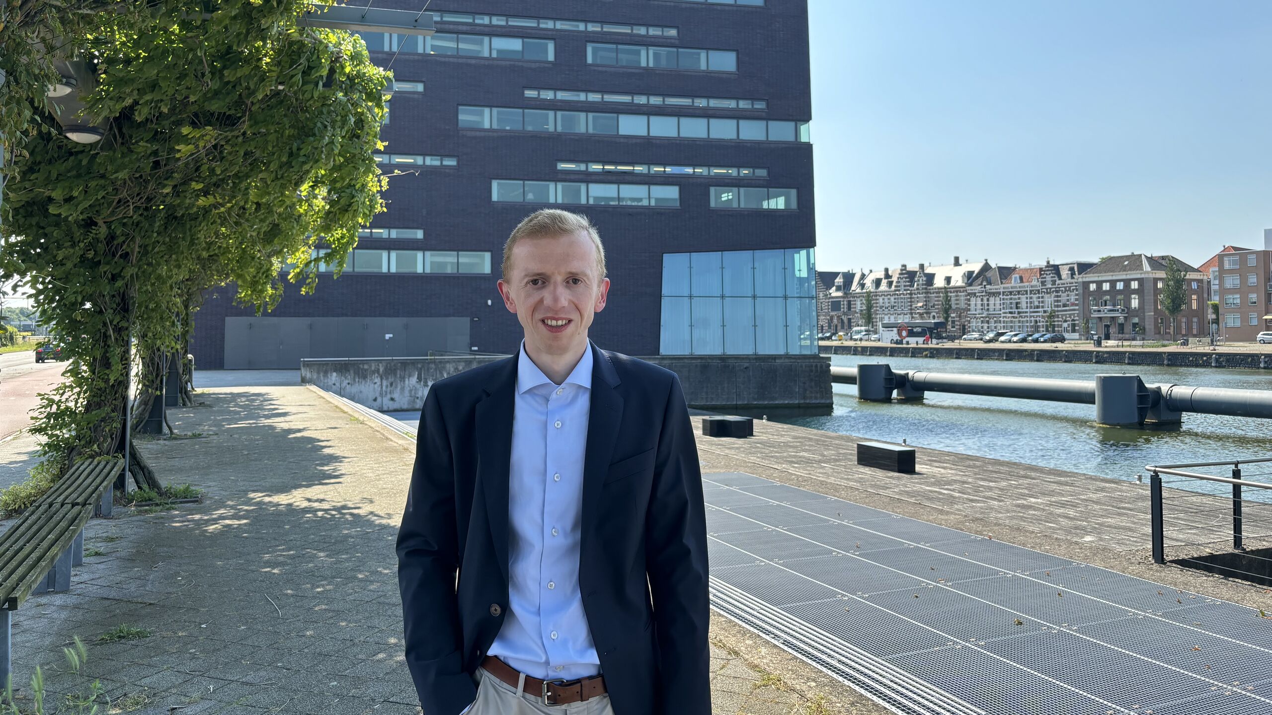 Collega Alexander staat lachend voor het waterschapskantoor.