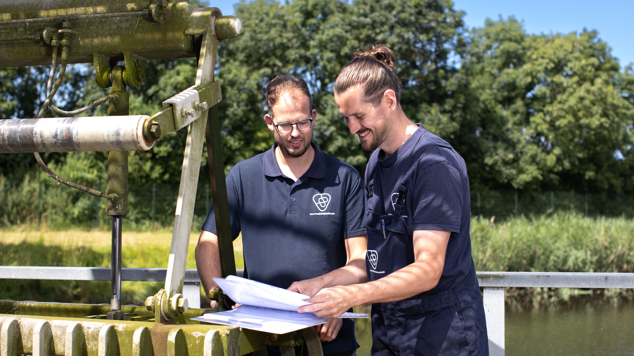 twee collega's staan buiten lachend op de foto en kijken naar een werkblad. 