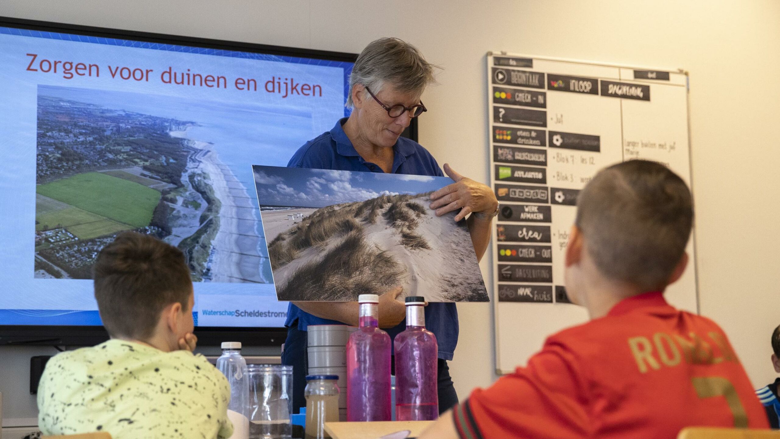 Een vrouw laat kinderen in de klas een foto van een duin zijn.