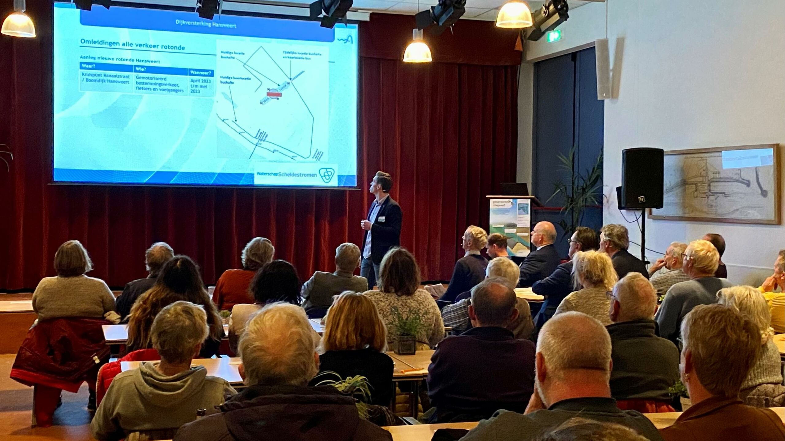 Mensen die in een zaal naar een presentatie kijken.