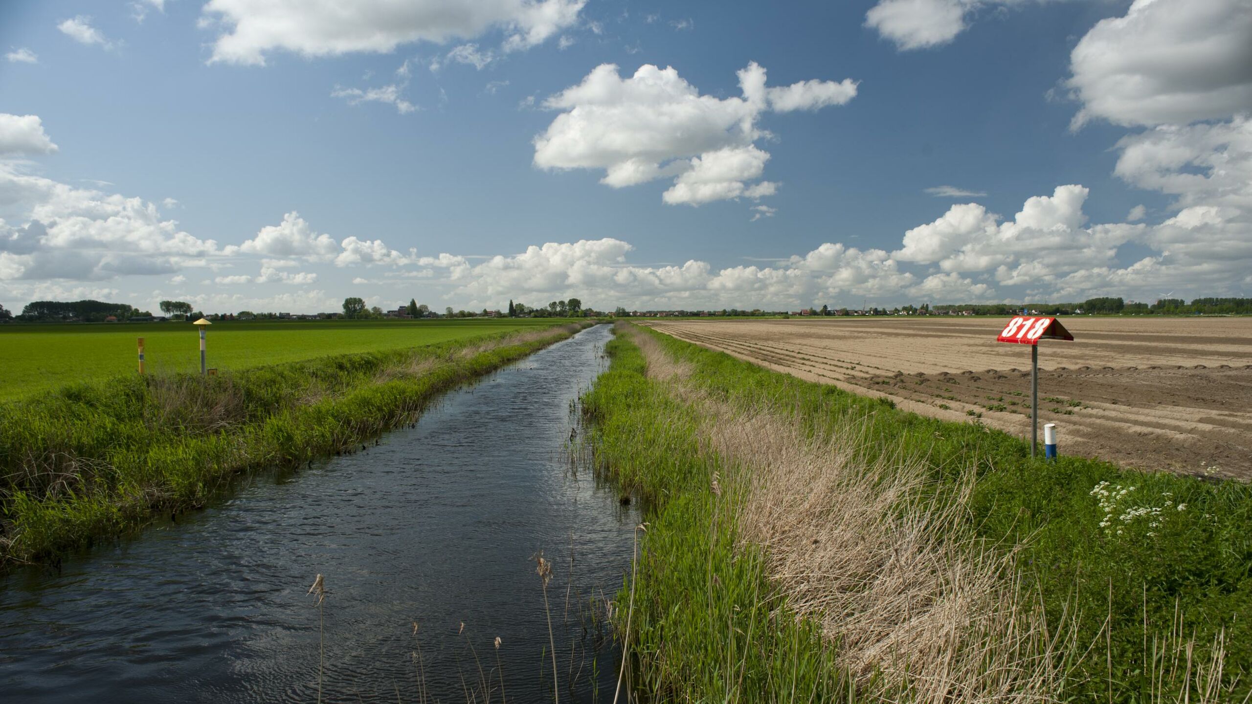 Een sloot naast een stuk land.