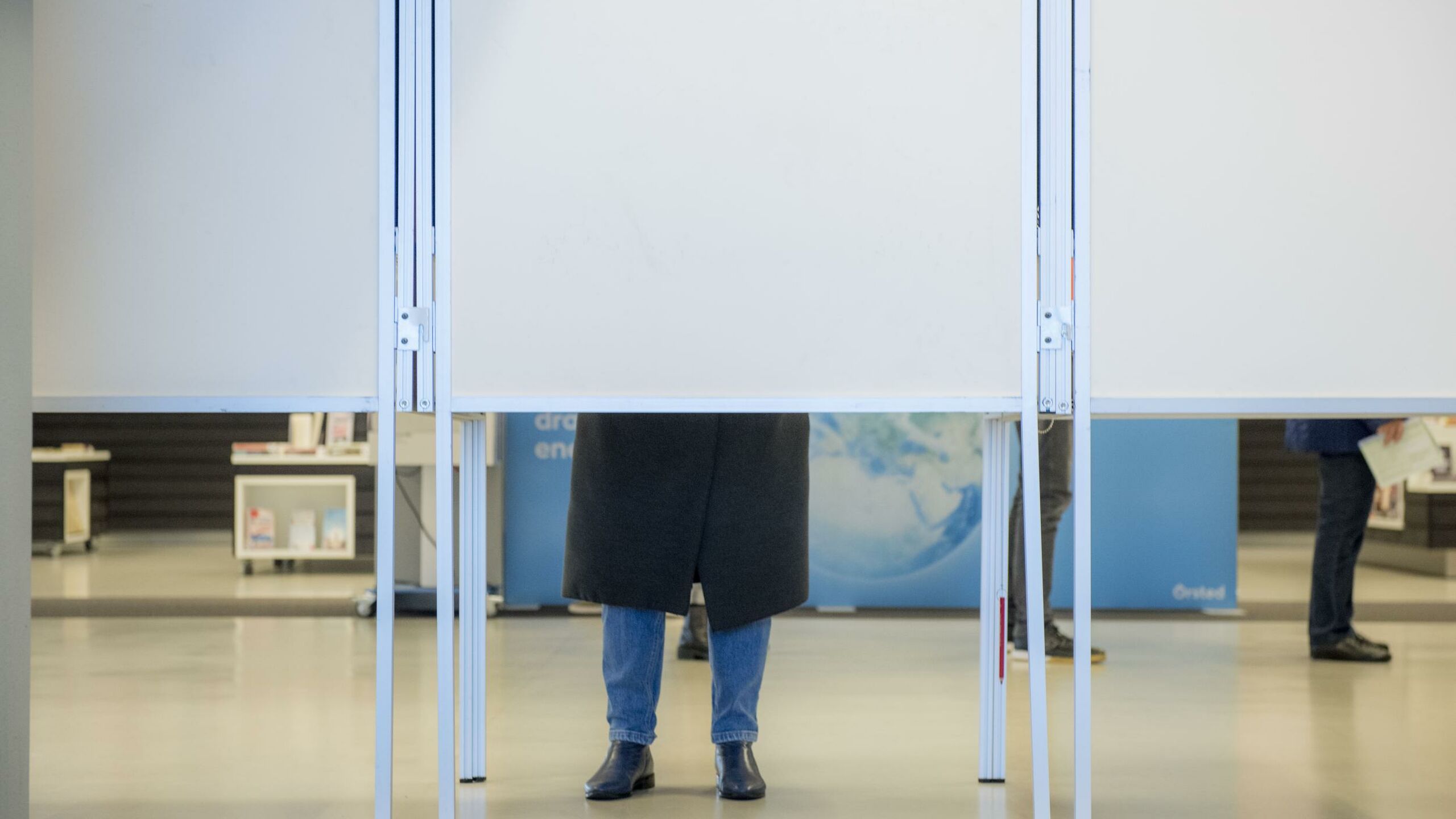 De achterkant van een stemhokje waar twee benen onderuit komen.