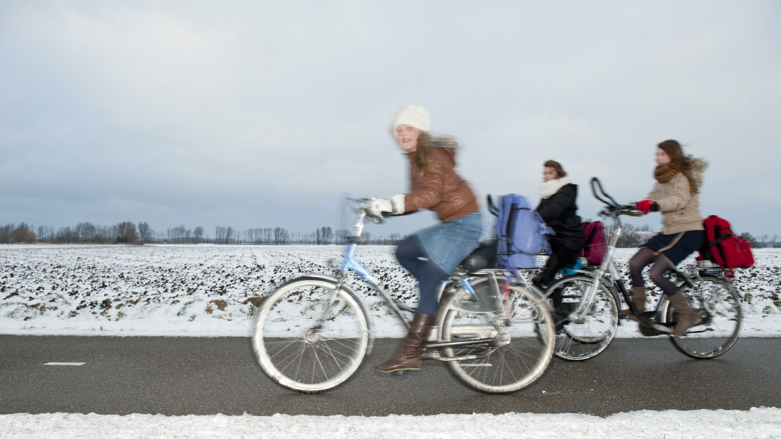 Scholieren fietsen over een fietspad door de sneeuw.