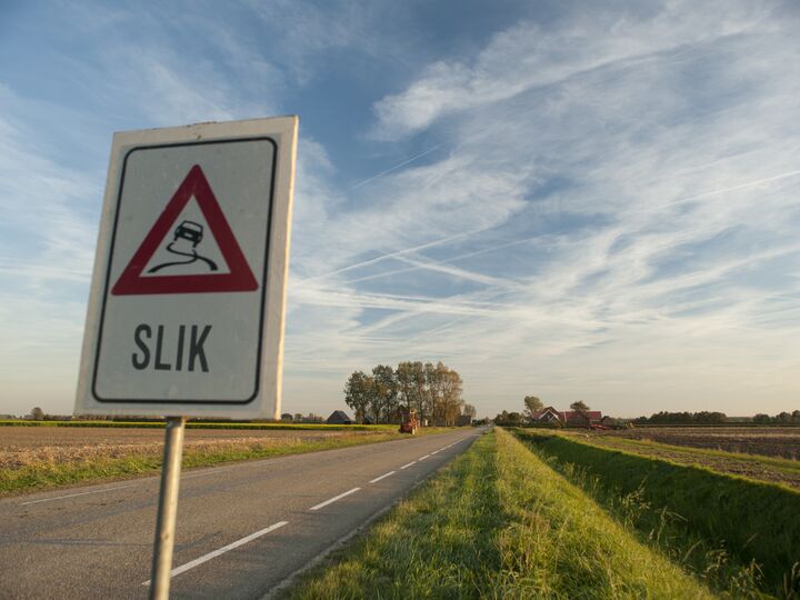 Een weg met een verkeersbord dat waarschuwt voor slik op de weg.