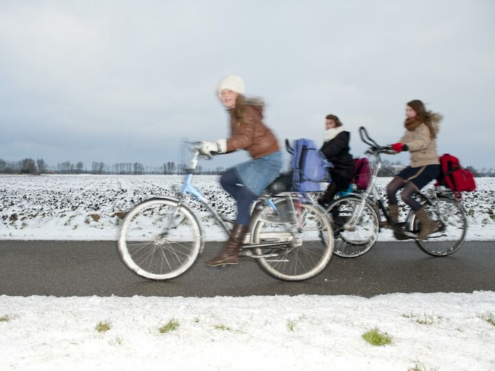 Scholieren fietsen over een fietspad door de sneeuw.