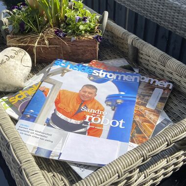 Een paar tijdschriften liggen op elkaar gestapeld op een dienblad op een tuintafel.