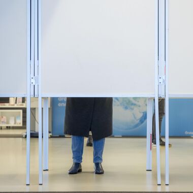 De achterkant van een stemhokje waar twee benen onderuit komen.