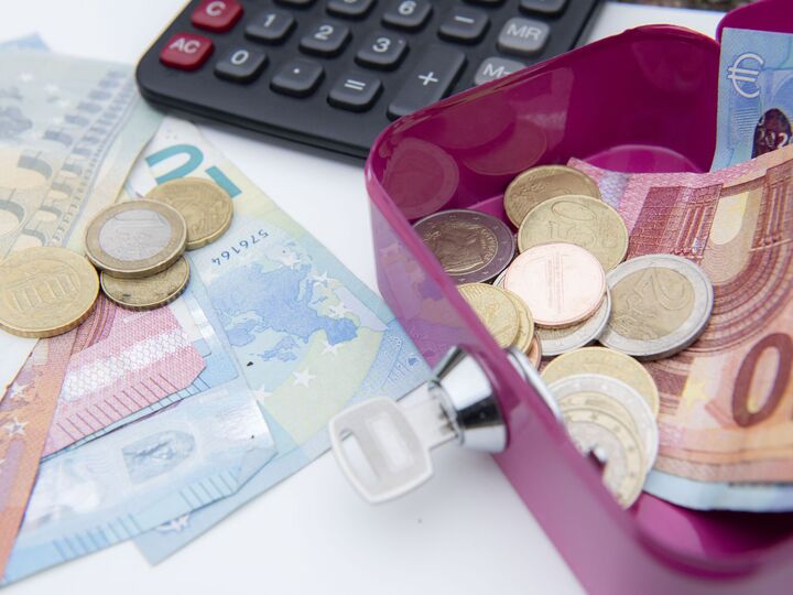 Euromunten en biljetten in een geldkistje met daarnaast een rekenmachine.